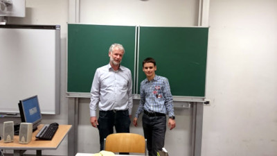 Photo of Marco Marinello standing next to a teacher with a green 
chalkboard in the background.